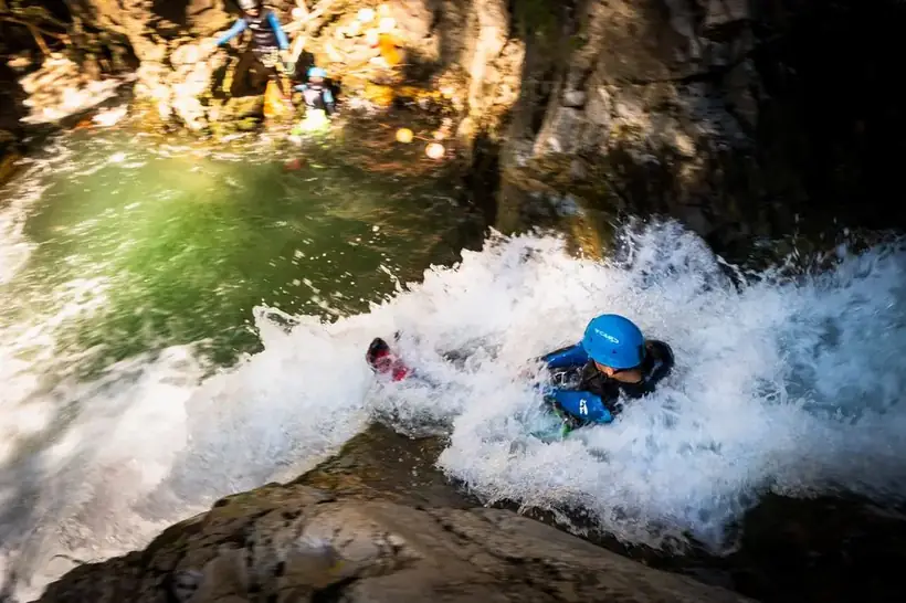 Canyoning guest sliding through whitewater into a plunge pool