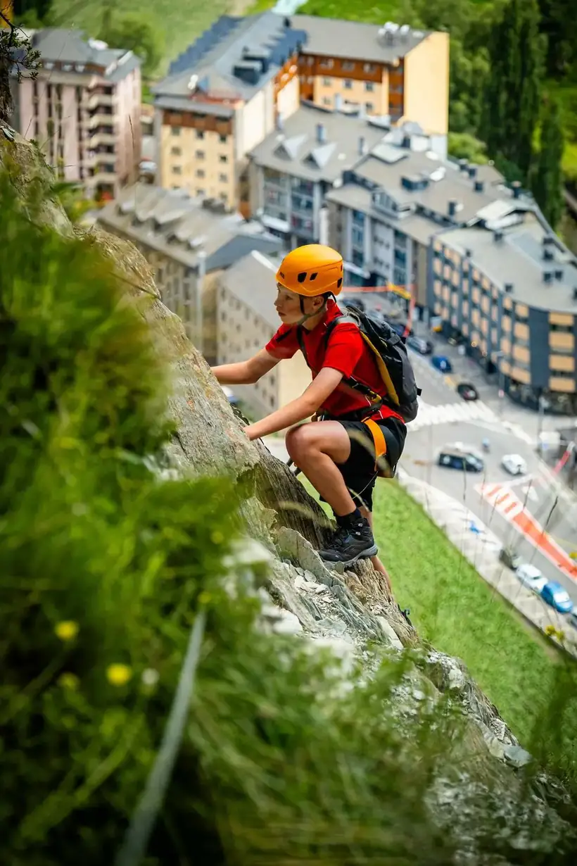 Boy climbing a via ferrata route with the town of Andorra la Vella spread out below