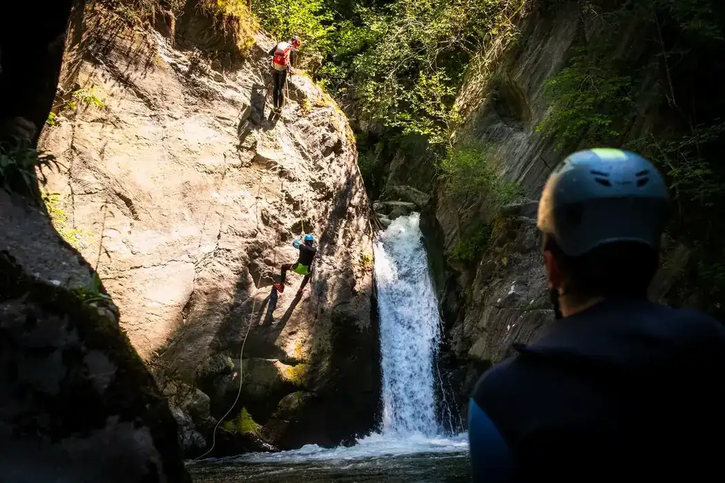 Canyoning guide abseiling down a rock face into a canyon in Andorra, watched by the group below