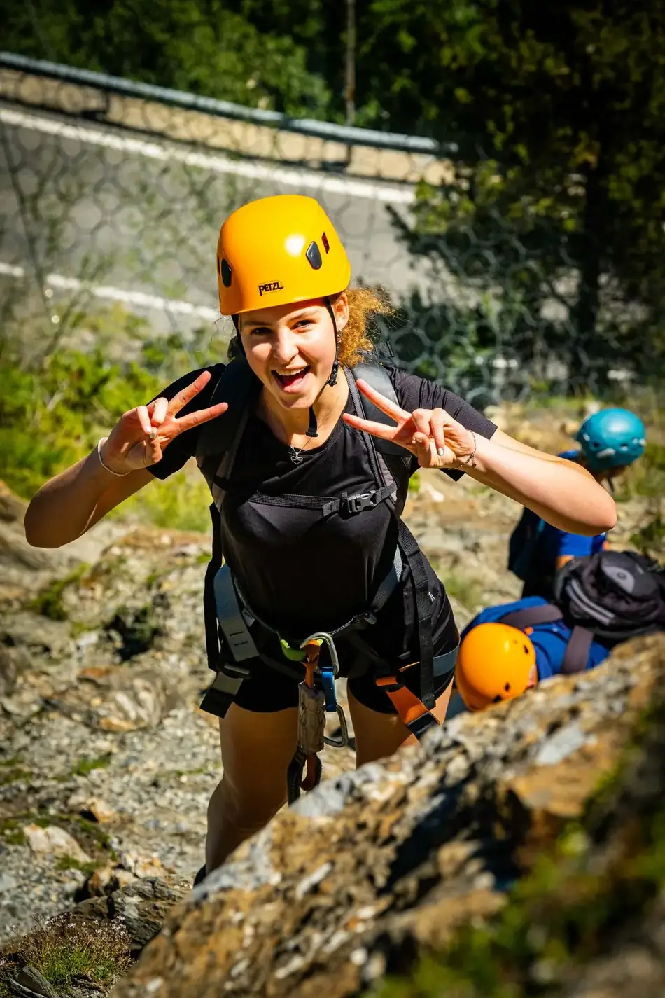Two people roped up and smiling on a via ferrata route in Andorra, one giving a peace sign